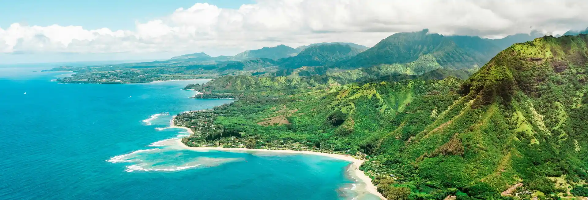 Stunning aerial view of a lush green mountain coastline meeting turquoise ocean, used as the Trips for Everyone hero image on Ghumora