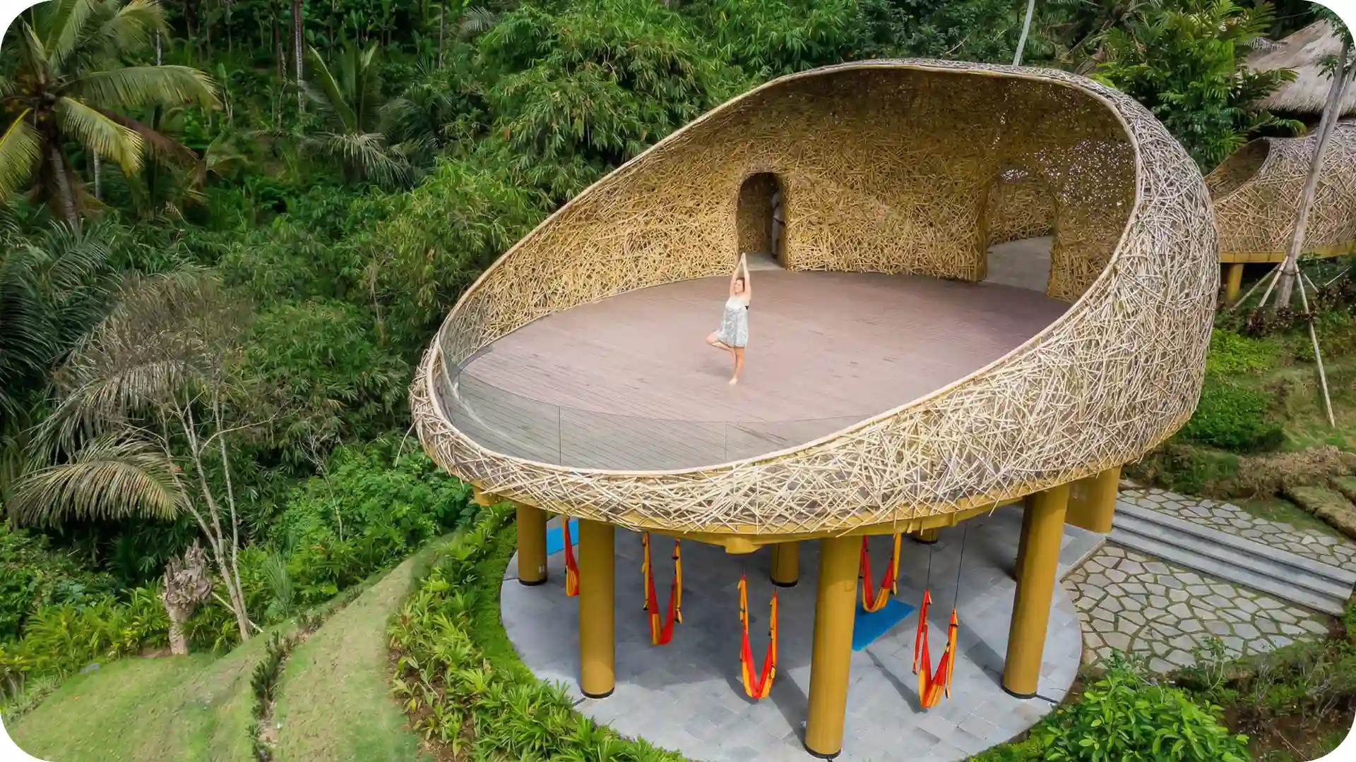 Aerial view of Bali yoga retreat with woman practicing on bamboo jungle deck, surrounded by lush tropical forest and serene mindful wellness setting