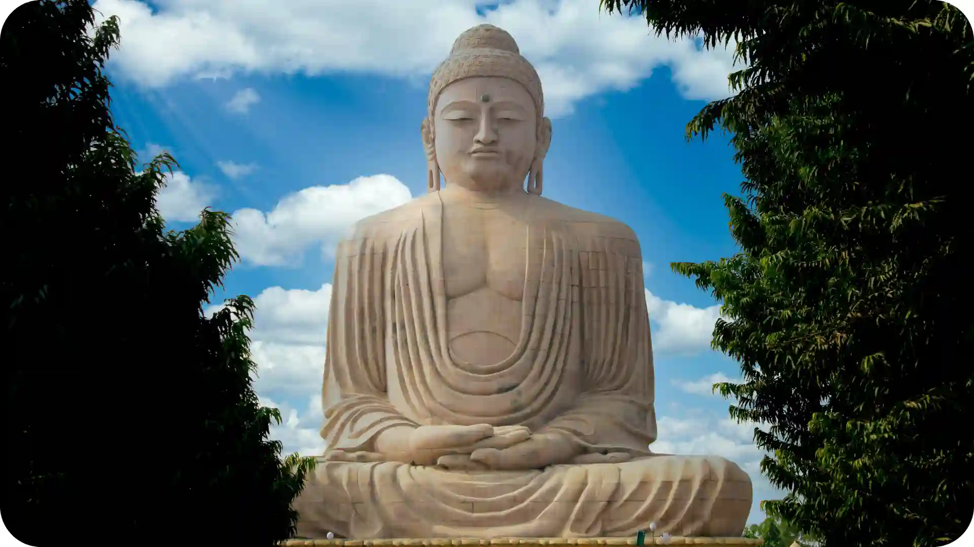 Great Buddha statue at Bodh Gaya in Bihar framed by trees under blue sky and clouds, symbolising India’s iconic Buddhist pilgrimage site