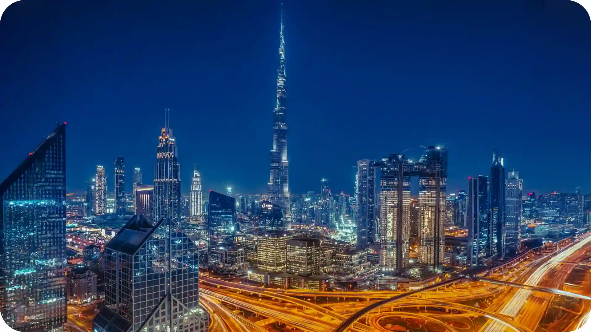 Dubai night skyline with Burj Khalifa towering over illuminated skyscrapers, shimmering waterfront reflections, and vibrant luxury city lights – Ghumora premium urban escape