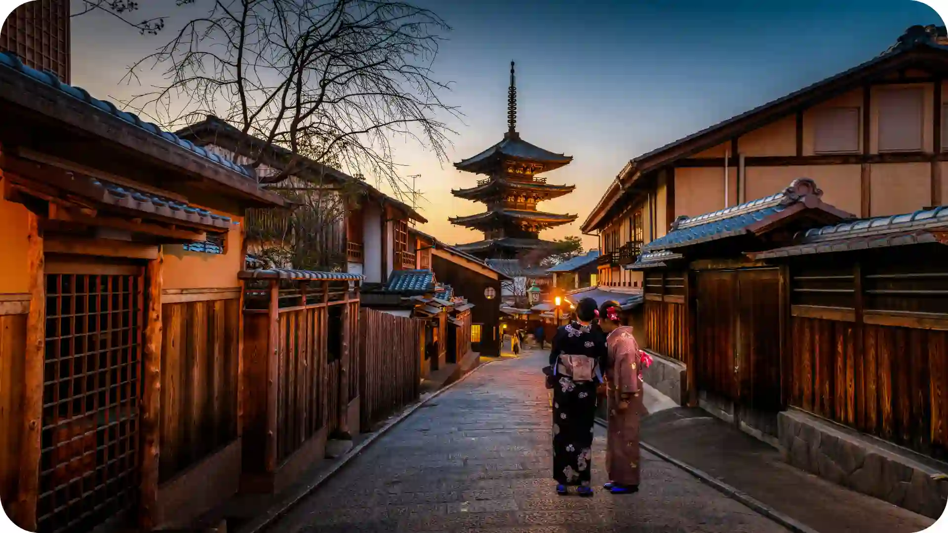 Yasaka Pagoda in Kyoto Japan rising above a narrow traditional wooden street at blue-hour evening, softly lit lanterns and warm lights – Ghumora cultural city stroll experience