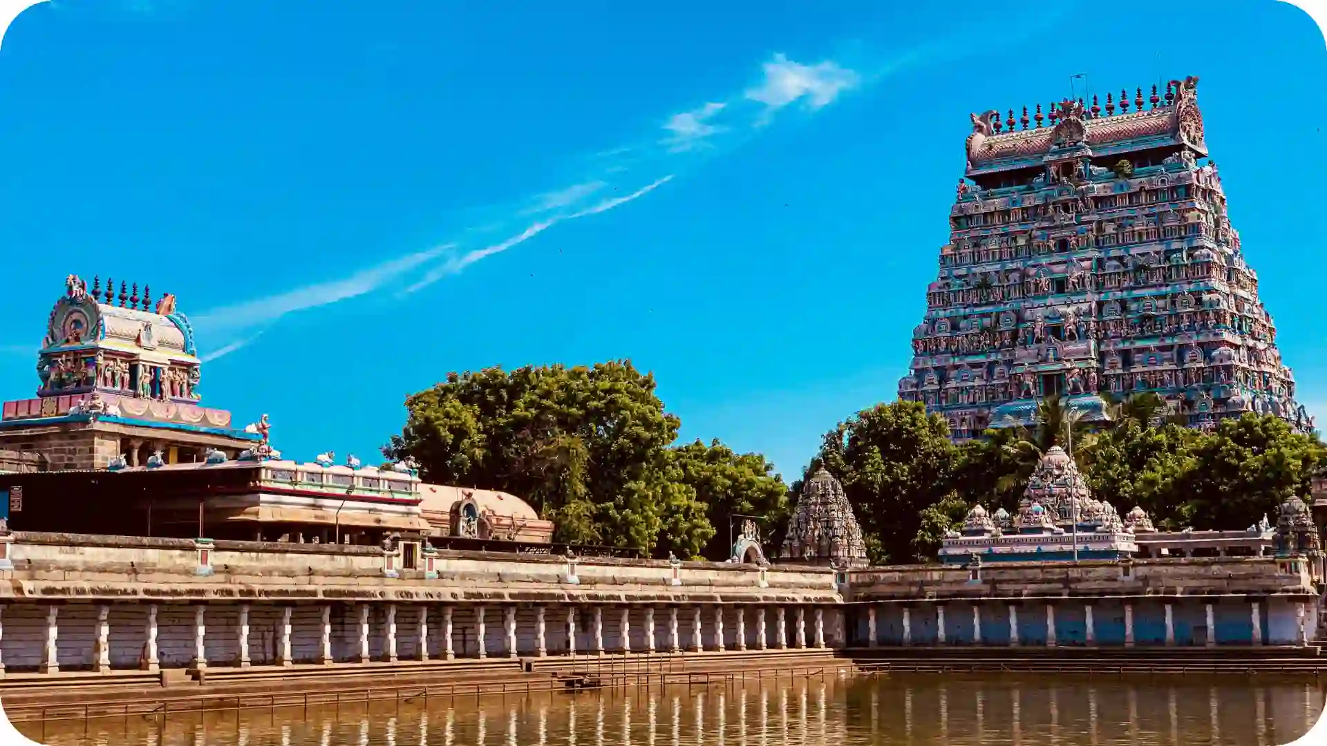 Colorful Dravidian temple gopuram rising above sacred tank in South India, reflecting intricate carvings, heritage architecture and spiritual pilgrimage atmosphere