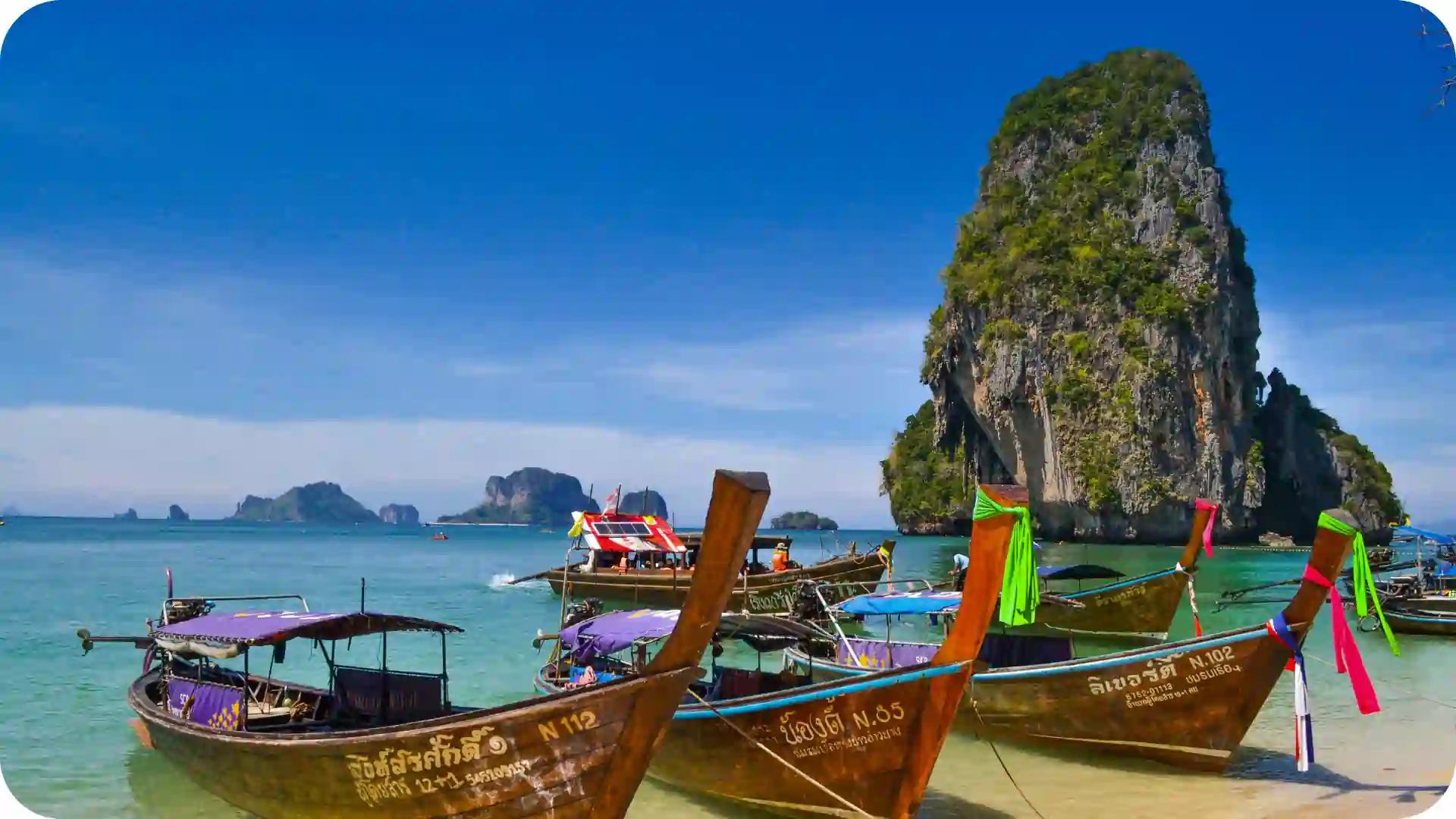 Long-tail boats on the sand at Railay Beach with limestone cliffs and blue sea in Krabi, Thailand, featured on Ghumora’s Thailand island hopping tour package