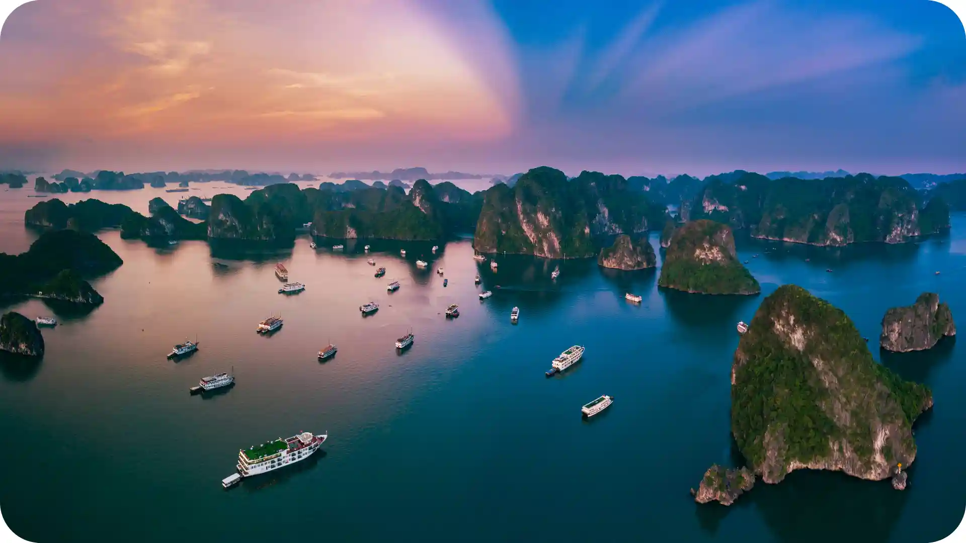 Ghumora Halong Bay cruise: aerial view of emerald waters with limestone karsts and traditional junk boats at golden hour sunset, representing luxury Vietnam adventure and scenic boat tours